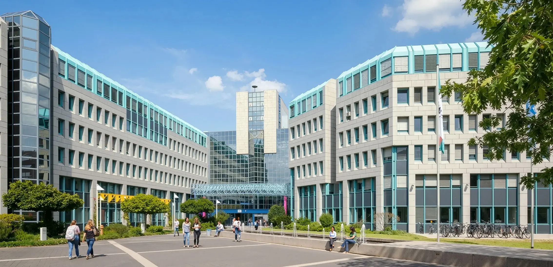 Moderner Bürokomplex mit Glasfassade, Bäumen und Spaziergängern an einem sonnigen Tag.